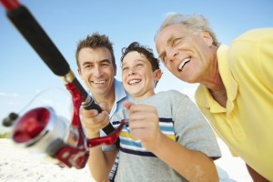 Cheerful little boy with his father and grandfather fishing on the beach